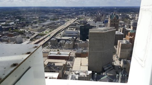 Aerial view of a city skyline featuring tall buildings and a highway, with a clear blue sky above.