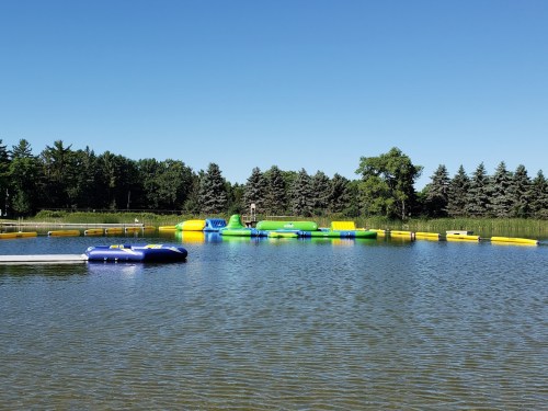 A colorful inflatable water park on a lake, surrounded by trees and clear blue skies.