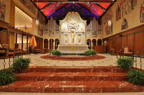 Interior of a grand church featuring an ornate altar, colorful murals, and elegant wooden furnishings.