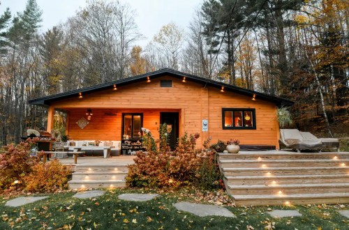 Cozy wooden cabin surrounded by autumn foliage, featuring a welcoming porch and warm outdoor lighting.