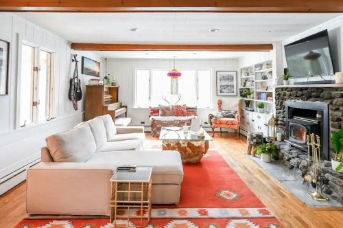 Cozy living room with a white sofa, wooden beams, stone fireplace, and colorful decor, featuring a warm, inviting atmosphere.