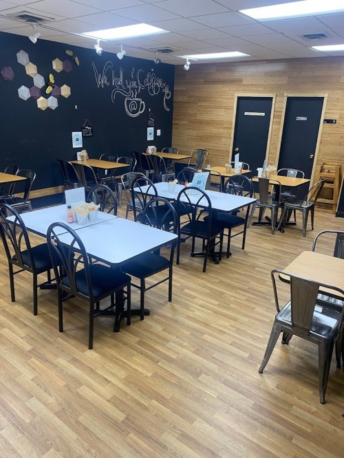 A cozy café interior with wooden floors, empty tables, and a chalkboard wall featuring a welcoming message.