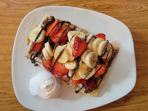 A plate of waffles topped with sliced strawberries, bananas, chocolate drizzle, and a scoop of whipped cream.