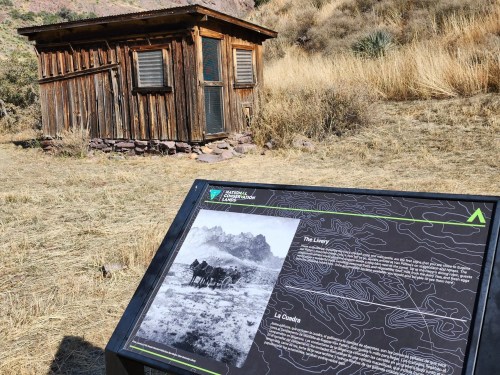 A wooden structure in a grassy area, with an informational sign about the site nearby.