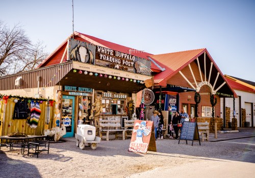 A rustic trading post with festive decorations, featuring shops and a slush puppy stand in a sunny outdoor setting.