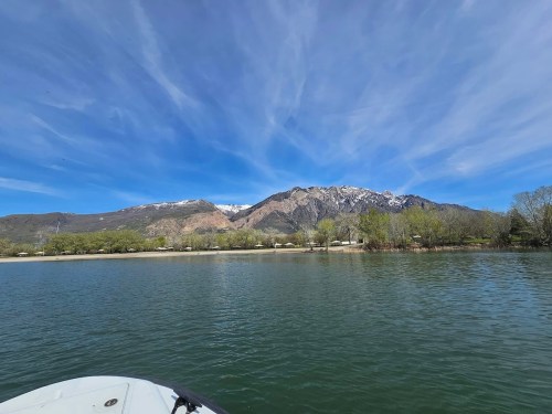 A serene lake view with mountains in the background, featuring clear blue skies and scattered clouds.