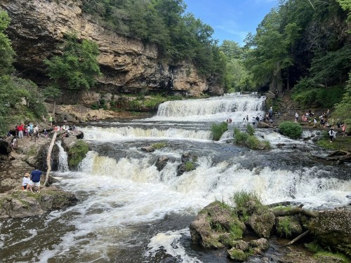 A scenic waterfall surrounded by lush greenery, with people enjoying the water and the natural landscape.