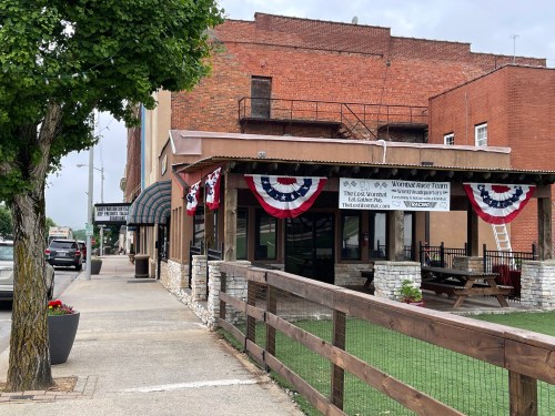 A street view of a building with patriotic decorations, featuring a patio and a sign for a local restaurant.