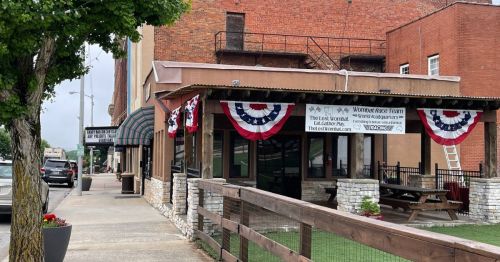 A street view of a building decorated with patriotic bunting, featuring outdoor seating and a wooden fence.