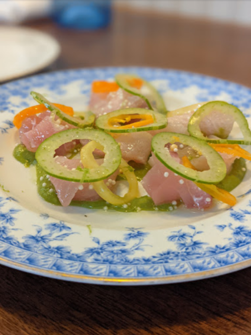 A colorful dish featuring sliced fish, garnished with green and yellow peppers, served on a decorative blue and white plate.