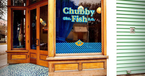 Exterior of Chubby Fish restaurant, featuring a wooden entrance and blue curtains, with a decorative tile floor.