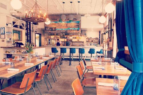A modern restaurant interior with wooden tables, blue chairs, and an open kitchen, featuring warm lighting and decor.