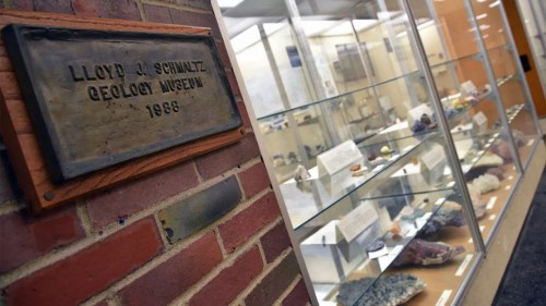 Plaque for Lloyd A. Schultz Geology Museum, with display cases of various geological specimens in the background.