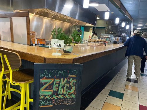 A cozy café interior with a wooden counter, a welcome sign, and patrons enjoying the space.