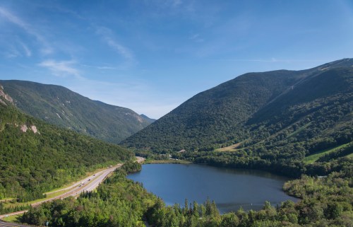 A serene landscape featuring a lake surrounded by lush green mountains under a clear blue sky.