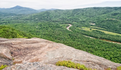 A panoramic view of lush green mountains and a winding river from a rocky overlook.