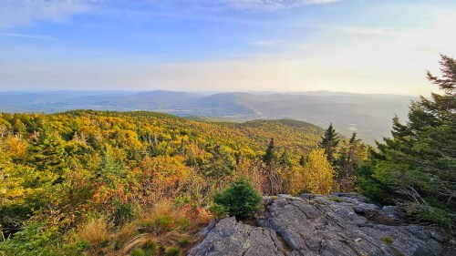 A scenic view of rolling mountains covered in autumn foliage under a clear blue sky.