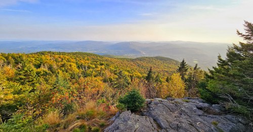 A scenic view of rolling mountains covered in autumn foliage under a clear blue sky.