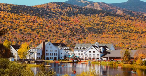 A scenic view of a lakeside resort surrounded by vibrant autumn foliage and mountains in the background.