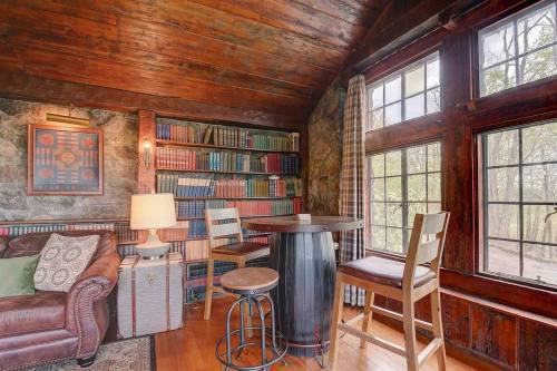 Cozy reading nook with a leather sofa, bookshelves, and a small table by large windows in a rustic wooden room.
