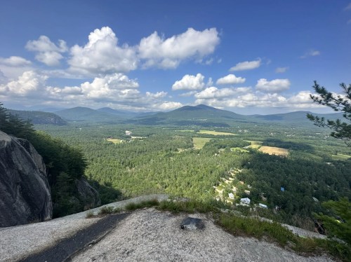 A panoramic view of lush green valleys and mountains under a partly cloudy sky.