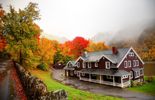 A charming red house surrounded by vibrant autumn foliage and misty mountains, with a winding road in the foreground.