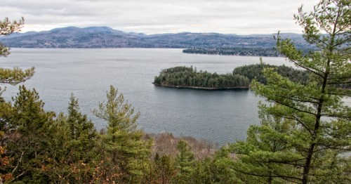 A serene lake surrounded by mountains and lush green trees, with a small island in the center.