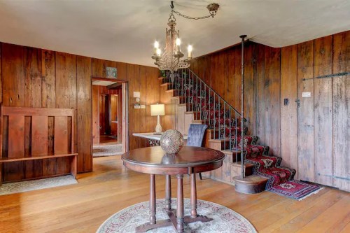 Cozy interior with wooden walls, a round table, and a staircase leading to an upper level, featuring a chandelier.