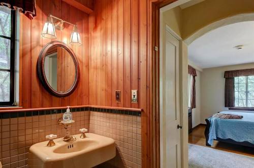 Cozy bathroom with wooden walls, a round mirror, and a vintage sink, leading to a softly lit bedroom.