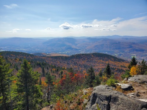 A scenic view of mountains and valleys, showcasing vibrant autumn foliage under a clear blue sky.