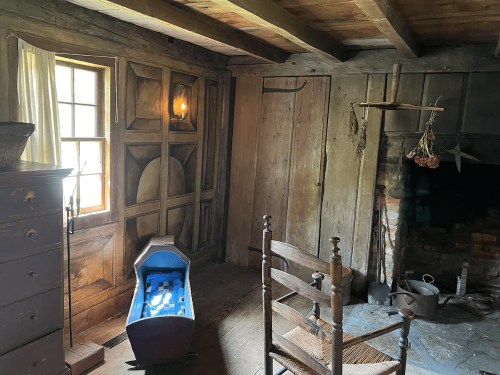 Cozy, rustic room with wooden walls, a crib, a chair, and a fireplace, illuminated by a lantern.