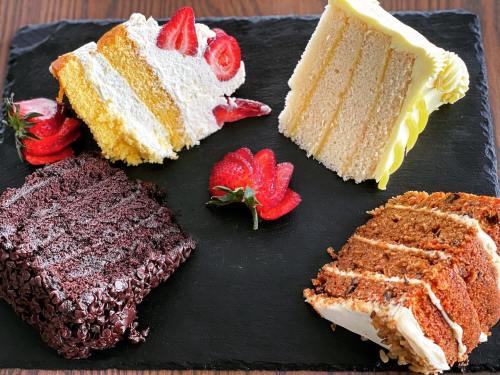 Four slices of cake on a slate platter: chocolate, vanilla, yellow, and red velvet, garnished with fresh strawberries.