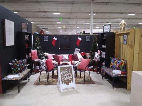 Cozy holiday-themed display with festive decorations, seating, and stockings in a spacious indoor setting.