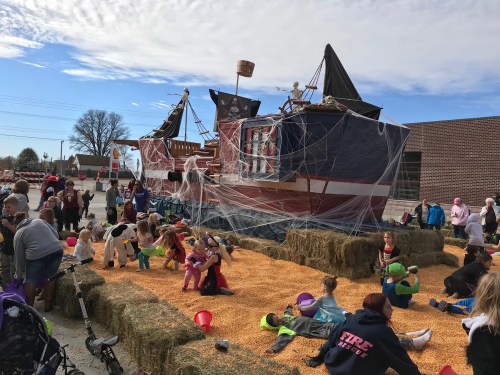 A festive scene with a pirate ship display, hay bales, and children in costumes enjoying a community event.