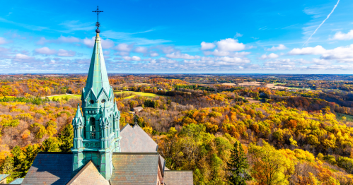 spire of the Holy Hill Basilica and National Shrine of Mary Help of Christians towers over the landscape filled with fall foliage in wisconsin