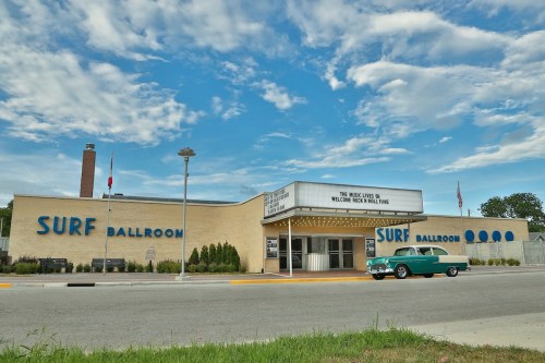 Exterior of the Surf Ballroom with a classic car parked outside, under a blue sky with scattered clouds.