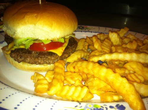 A cheeseburger with lettuce and tomato on a plate, accompanied by a side of crinkle-cut fries.