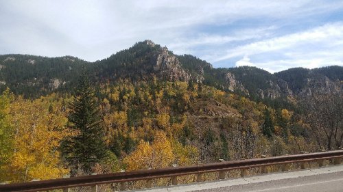 Scenic view of a mountain landscape with autumn foliage in vibrant yellow and green under a cloudy sky.