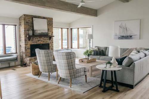 Cozy living room with stone fireplace, large windows, gray sofas, and stylish armchairs, featuring a light color palette.