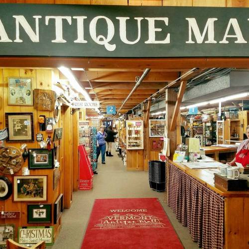 Interior of an antique market with wooden walls, displays of vintage items, and a welcome mat at the entrance.