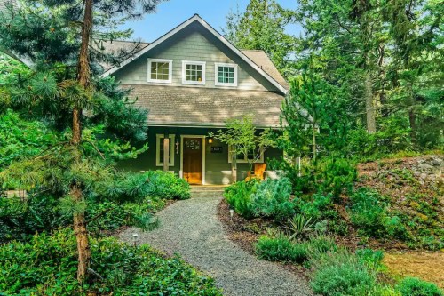 A charming green house surrounded by lush trees and a gravel path, set in a serene, natural landscape.