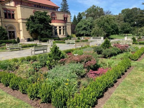 A landscaped garden with colorful flowers and greenery, benches, and a historic building in the background.