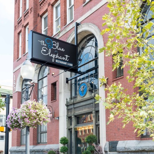 Exterior of The Blue Elephant Restaurant & Bar, featuring a sign and hanging flower baskets in a historic building.