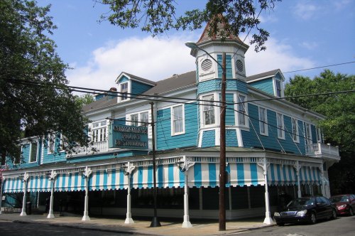 A large, blue Victorian-style building with white striped awnings and a tower, featuring a restaurant sign outside.