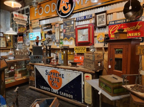 A vintage shop display featuring old signs, a wooden counter, and various antique items in a rustic setting.