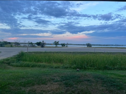 A serene landscape featuring a grassy foreground, a road, and a colorful sky at dusk with scattered clouds.