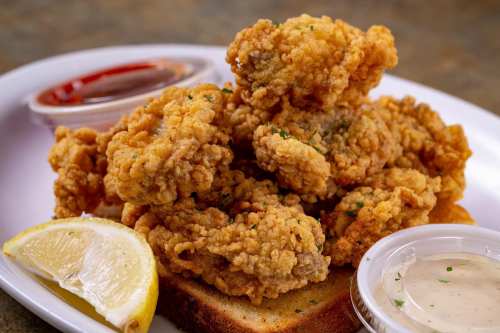 A plate of crispy fried chicken pieces on toast, served with lemon wedges and dipping sauces.
