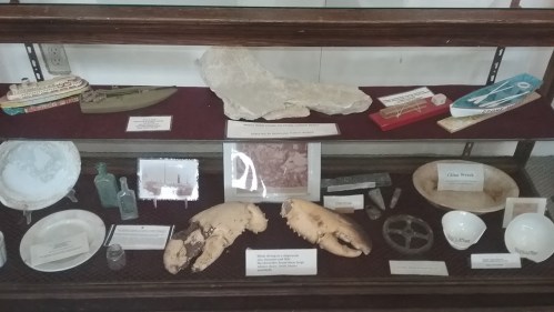Display case featuring various historical artifacts, including ship models, bottles, and pottery.