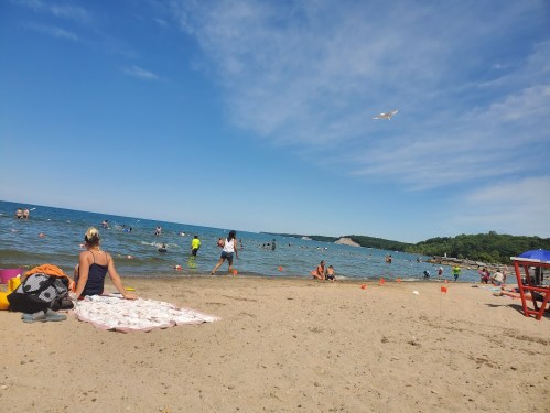 A sunny beach scene with people swimming, playing, and relaxing on the sand near the water's edge.