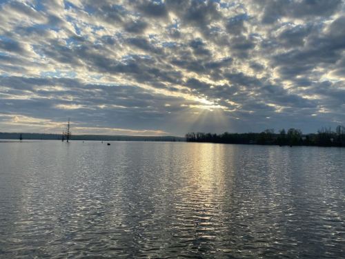A serene lake scene at sunset, with clouds reflecting on the water and rays of sunlight breaking through.